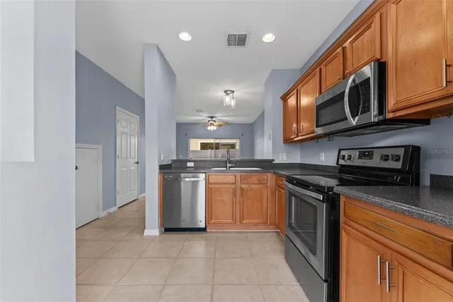 a kitchen with stainless steel appliances granite countertop a stove top oven a sink dishwasher and a refrigerator with wooden cabinets