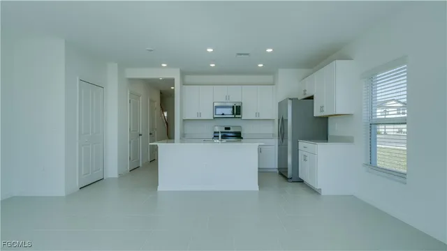 a large white kitchen with kitchen island a sink a refrigerator and white cabinets