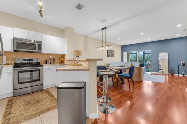 a kitchen with stainless steel appliances granite countertop a stove top oven a sink a dining table and chairs with wooden floor