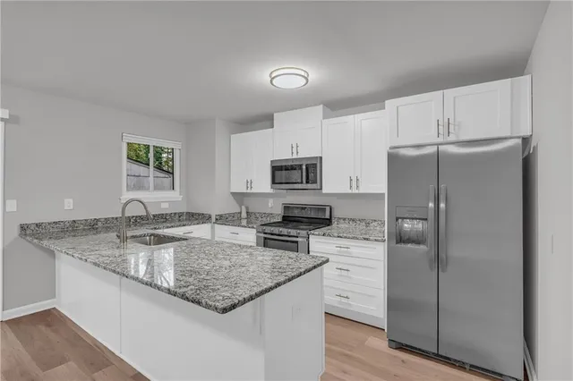 a kitchen with stainless steel appliances granite countertop a refrigerator a stove and a sink with wooden floor