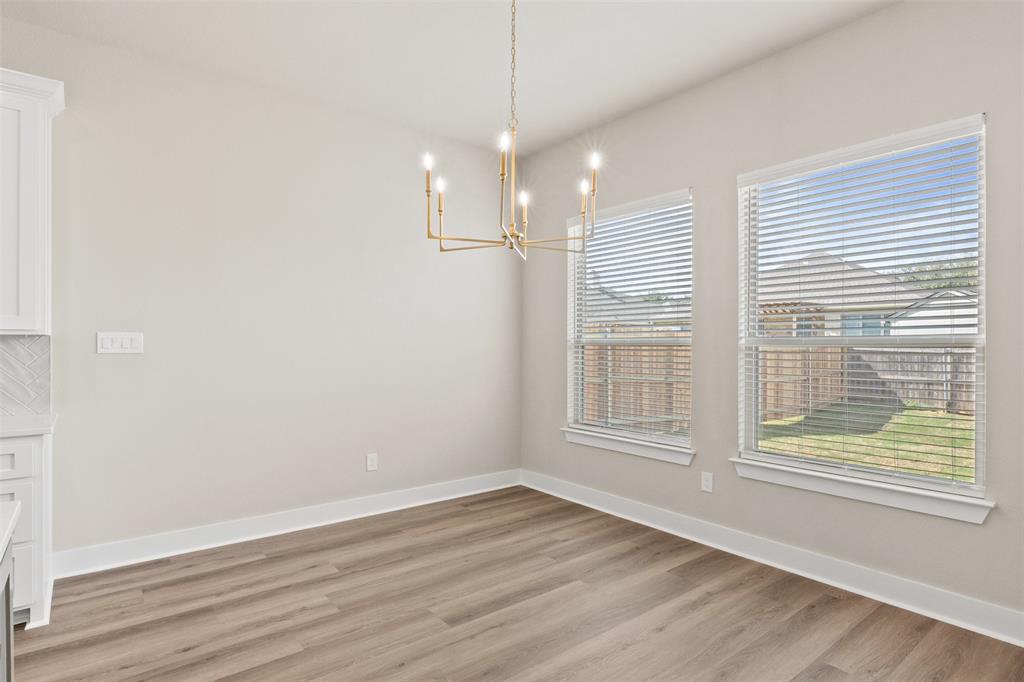 9824 Durango Trail Waco, TX 76712 - Photo 9 of 30 Dining area featuring wood-finish flooring, a modern gold-tone chandelier, two windows with blinds, and light-toned walls