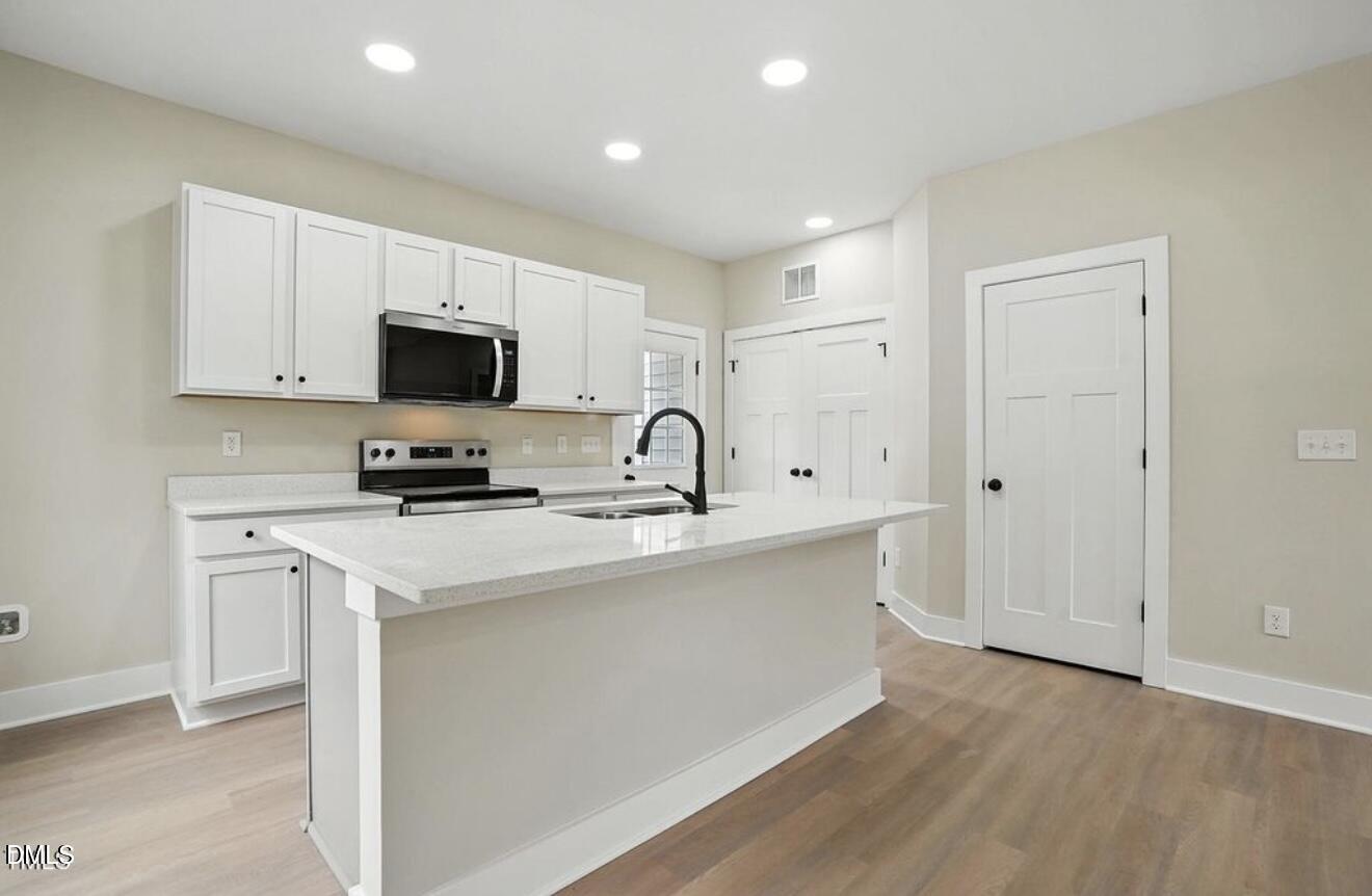 1240 West Blackman Road Dunn, NC 28334 - Photo 9 of 25 a kitchen with stainless steel appliances a sink a stove a microwave a refrigerator a white cabinets and wooden floor