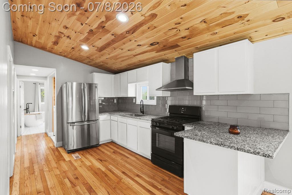 5698 McGrandy Road Bridgeport, MI 48722 - Photo 13 of 26 Kitchen featuring a wood-finish vaulted ceiling with recessed lighting, stainless steel refrigerator, black range with hood vent, white cabinetry, and granite-look countertops with a gray subway tile backsplash