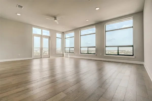 an empty room with wooden floor and windows with curtains