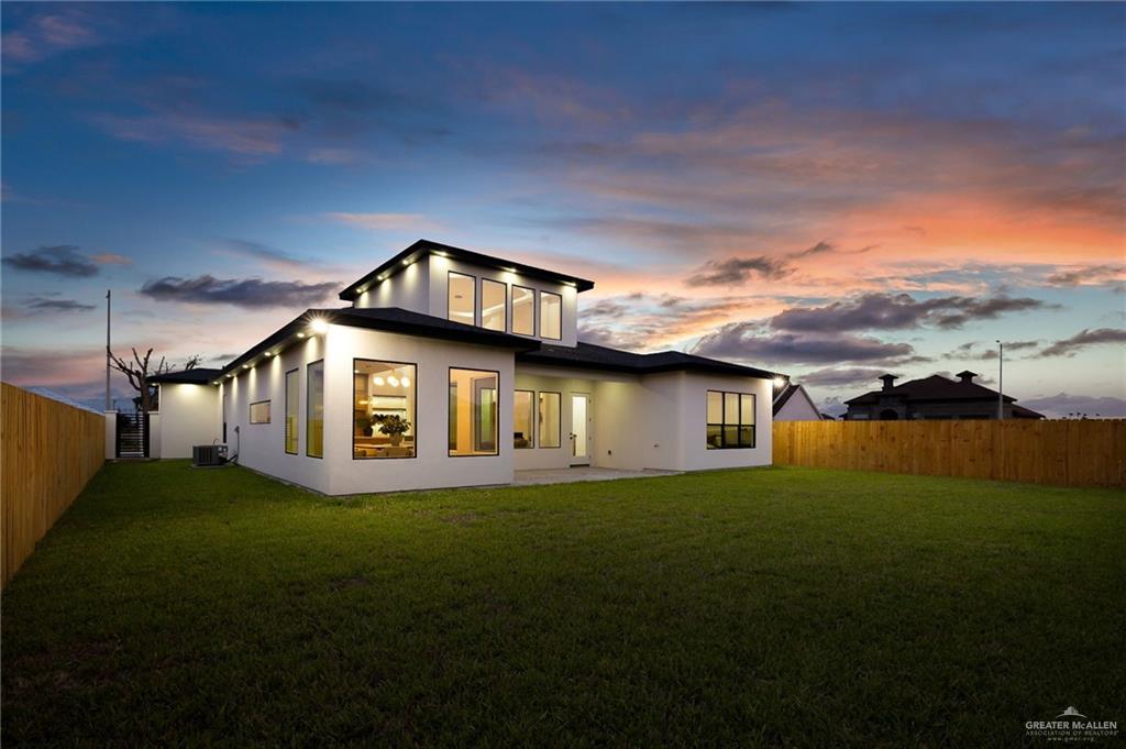 1107 Benjamin Street Mission, TX 78573 - Photo 3 of 19 Contemporary stucco exterior featuring a tiered roofline, expansive windows, recessed exterior lighting, and a private wooden fence enclosing a spacious green lawn
