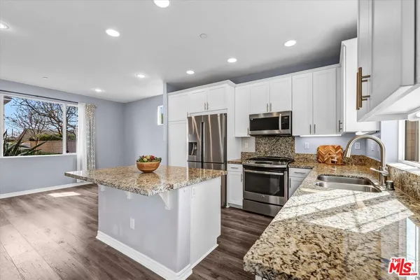 a kitchen with stainless steel appliances granite countertop a stove top oven a sink a refrigerator and white cabinets with wooden floor