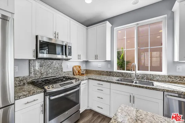 a kitchen with granite countertop white cabinets stainless steel appliances a window and a sink