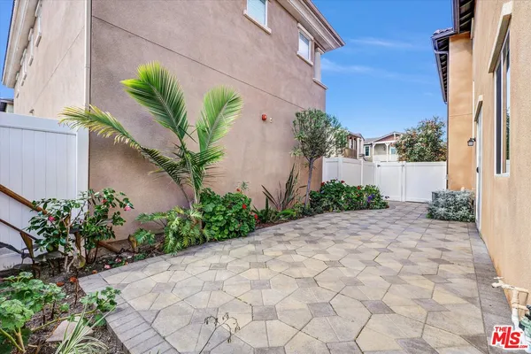 a sidewalk with a white house with potted plants in front of it
