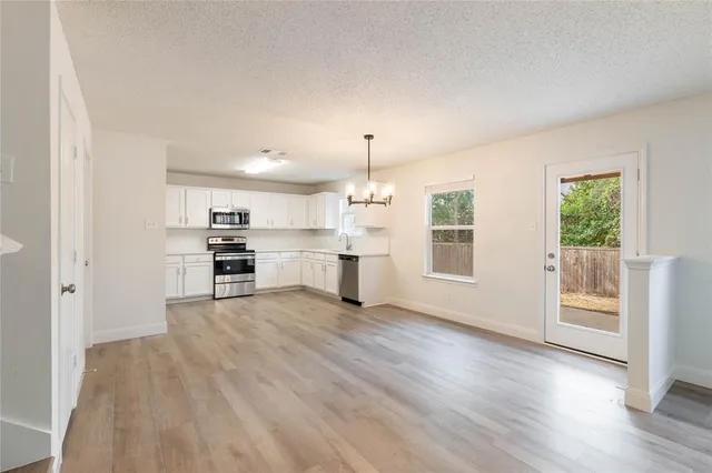 an empty room with wooden floor kitchen view and a window