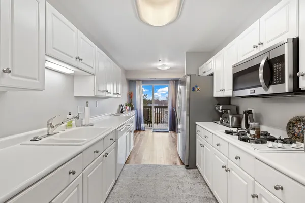 a large white kitchen with stainless steel appliances granite countertop a sink dishwasher a stove and a microwave oven with cabinets