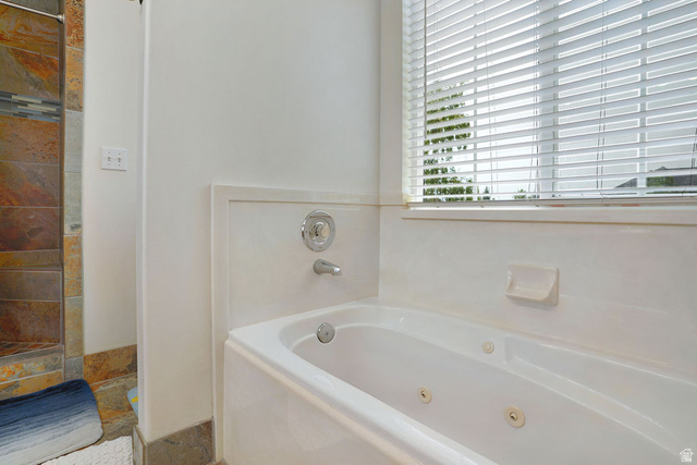 464 West Saddle Back Drive Springville, UT 84663 - Photo 11 of 15 Jetted soaking tub with chrome fixtures, complemented by a tiled shower surround featuring earth-toned stone and a decorative glass tile accent band