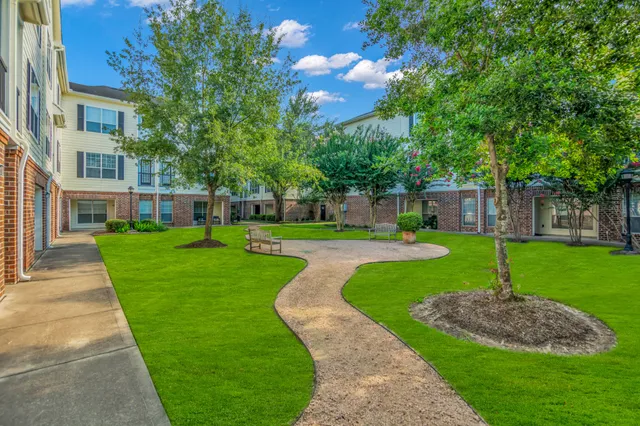 a view of a fountain in front of a brick house with a big yard and large trees