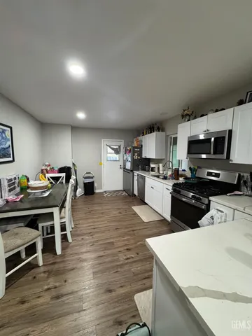 a kitchen with stainless steel appliances kitchen island granite countertop a stove top oven a sink a dining table and chairs with wooden floor