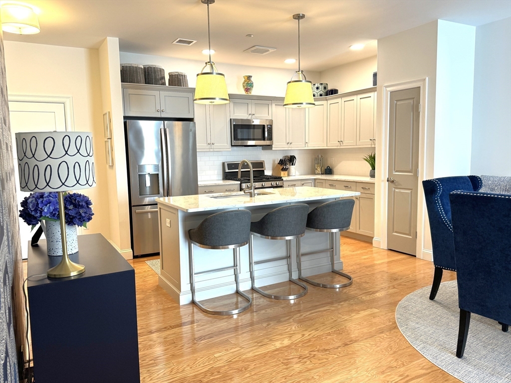 a kitchen with stainless steel appliances kitchen island granite countertop a dining table chairs and a refrigerator