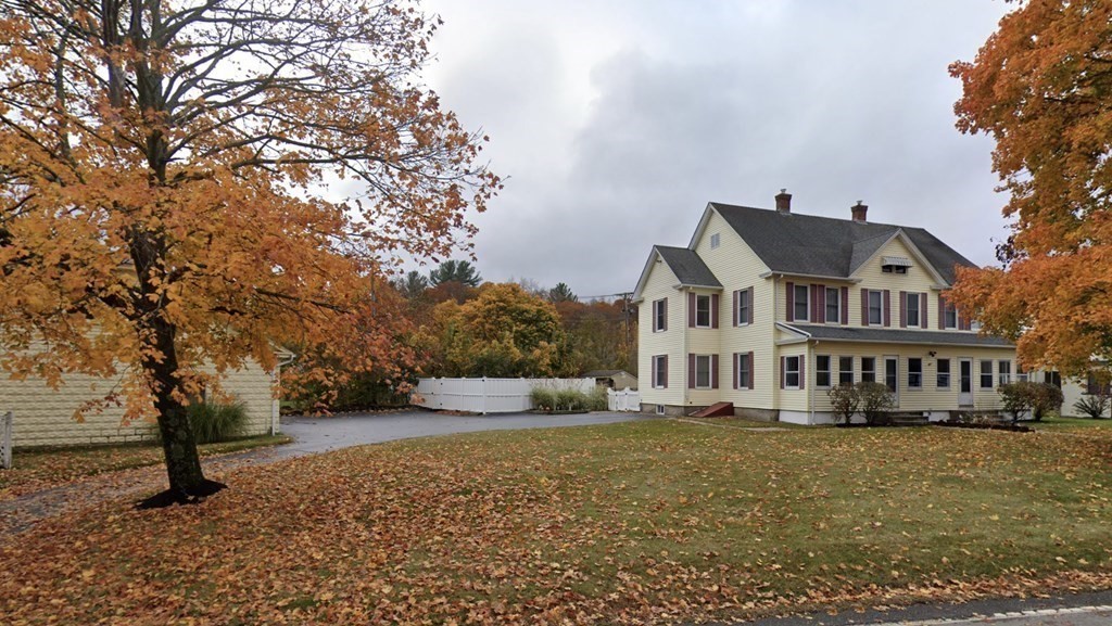 a front view of a house with large trees and houses