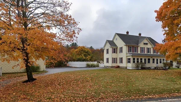 a front view of a house with large trees and houses