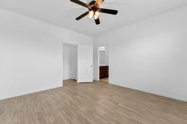 a view of an empty room with chandelier fan and wooden floor