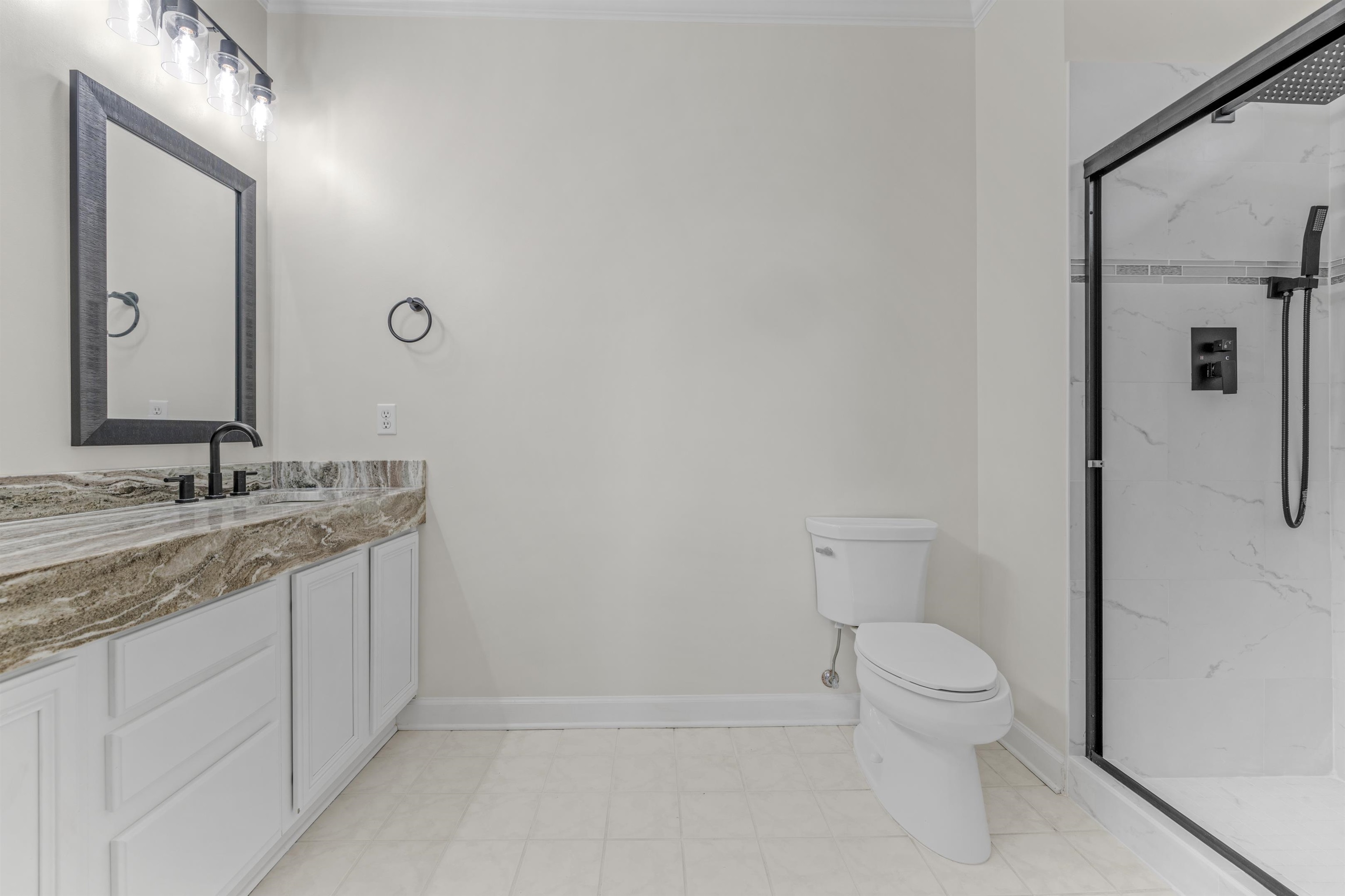 921 Harbor View Drive Memphis, TN 38103 - Photo 26 of 33 Bathroom featuring a vanity with a patterned countertop and white cabinetry, a framed mirror, a ceiling-mounted light fixture, and a glass-enclosed shower with a rainfall showerhead