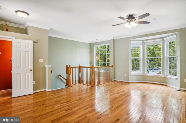 a view of an empty room with wooden floor and a ceiling fan