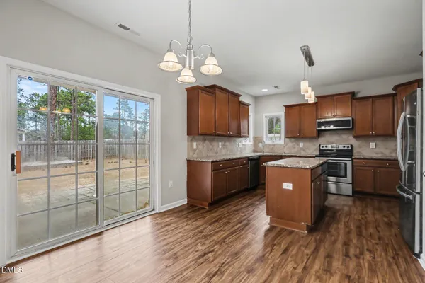 a large kitchen with stainless steel appliances granite countertop a stove a refrigerator a sink dishwasher a dining table and chairs with wooden floor