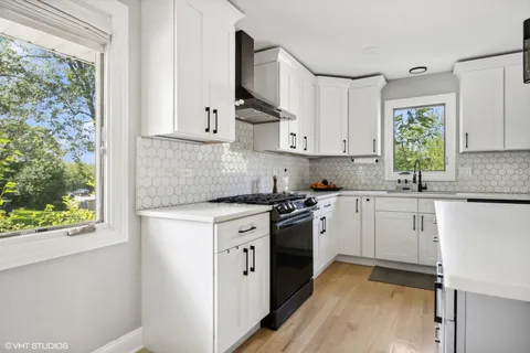 a kitchen with stainless steel appliances granite countertop a stove a sink and white cabinets with wooden floor