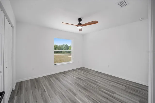 an empty room with wooden floor ceiling fan and windows