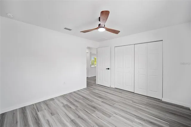 a view of an empty room with chandelier fan and wooden floor