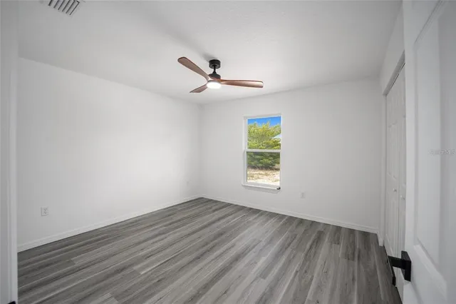 an empty room with wooden floor ceiling fan and windows