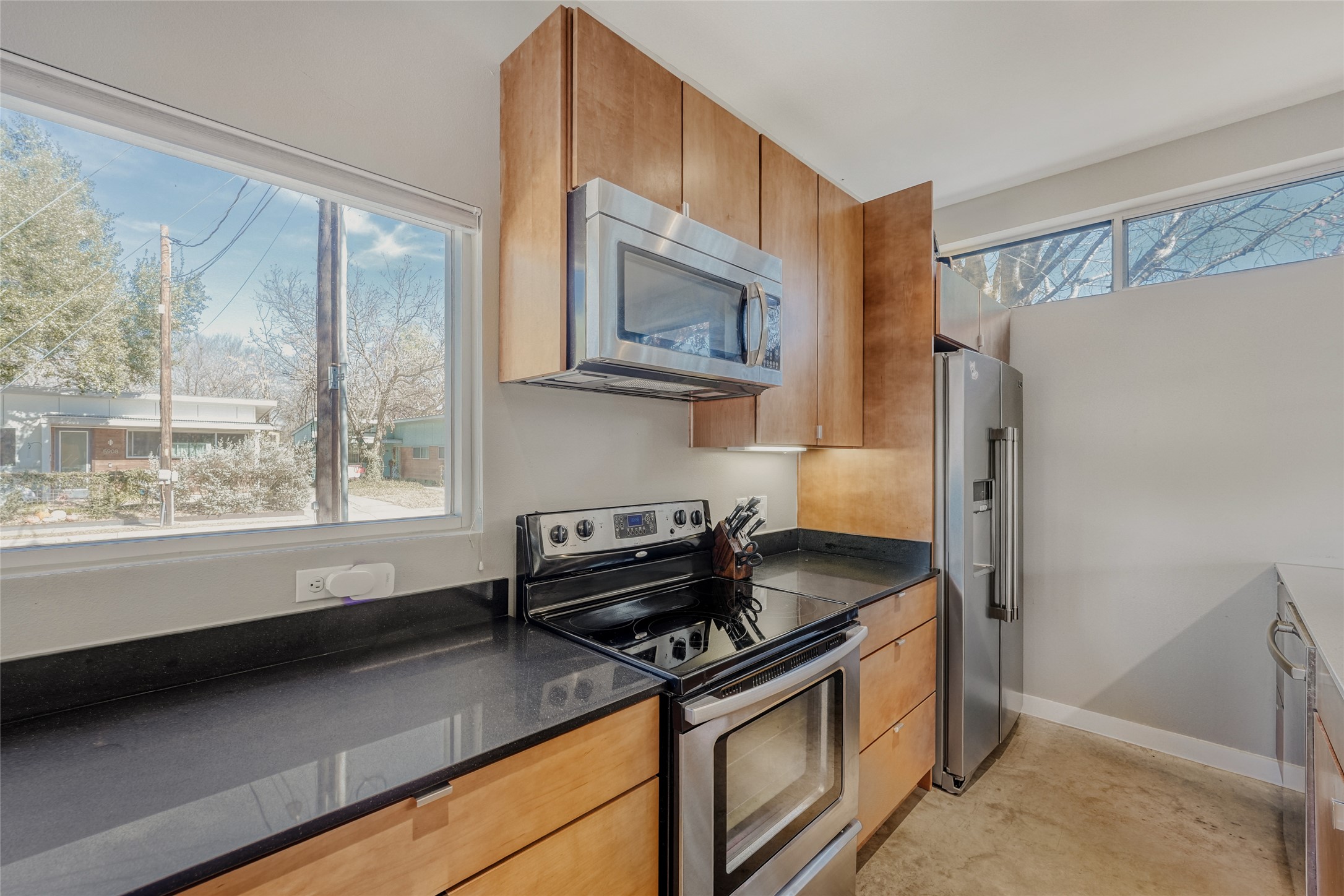 5909 Lux Street Austin, TX 78721 - Photo 11 of 28 Kitchen with stainless steel appliances, wood cabinetry, dark stone countertops, and concrete flooring