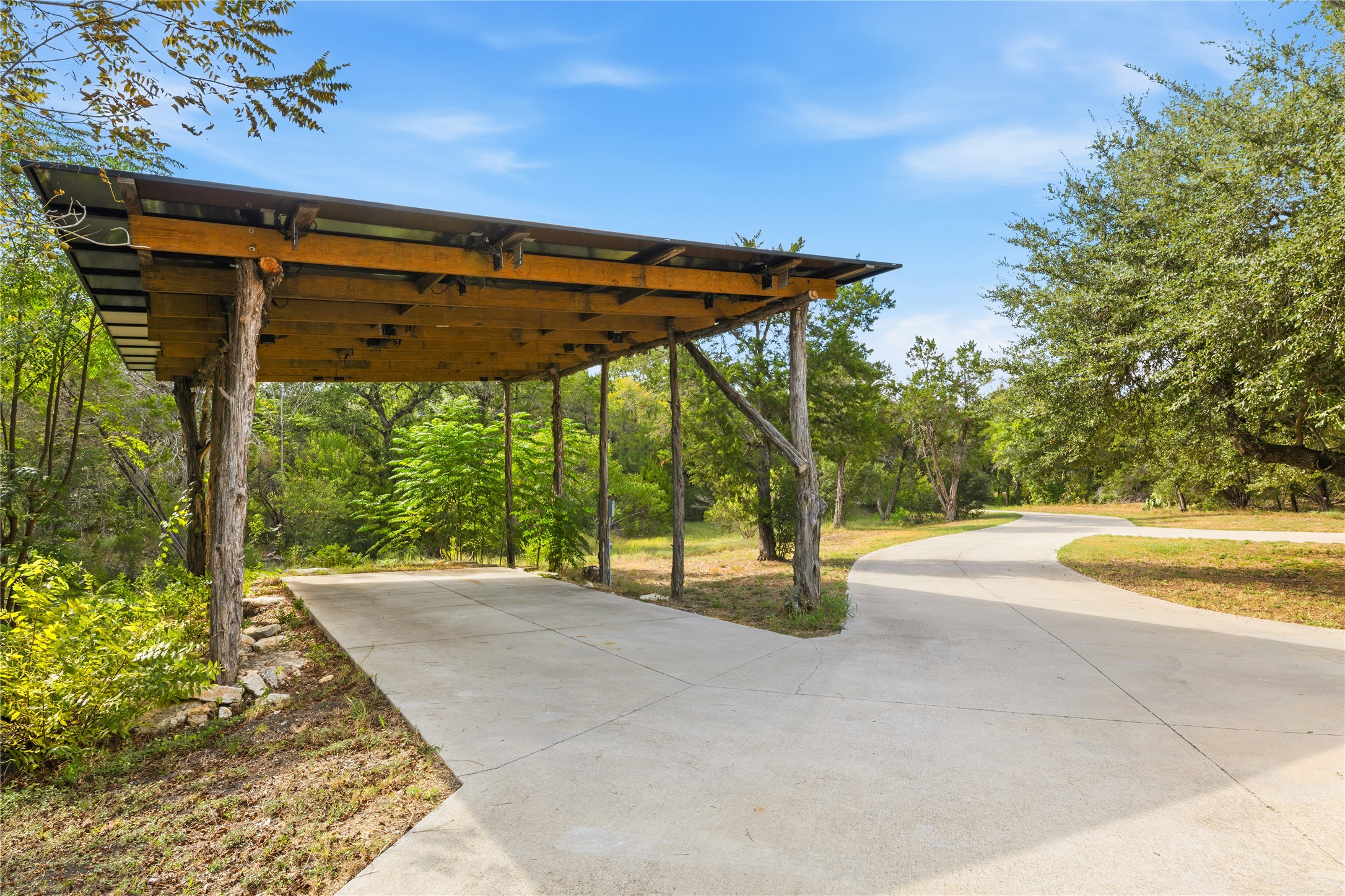 12901 Wire Road Leander, TX 78641 - Photo 30 of 40 Rustic wooden carport sits alongside a winding concrete driveway surrounded by mature trees.
