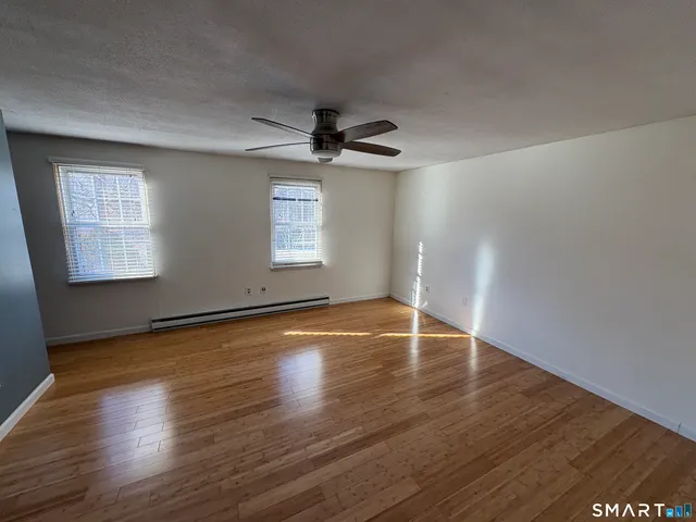 an empty room with wooden floor chandelier fan and windows