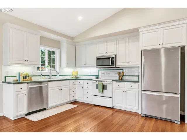 a kitchen with white cabinets appliances a sink and a window