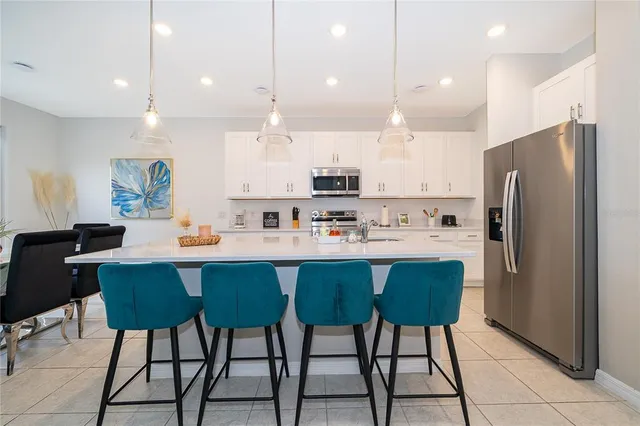 a kitchen with stainless steel appliances kitchen island granite countertop a dining table chairs and a refrigerator