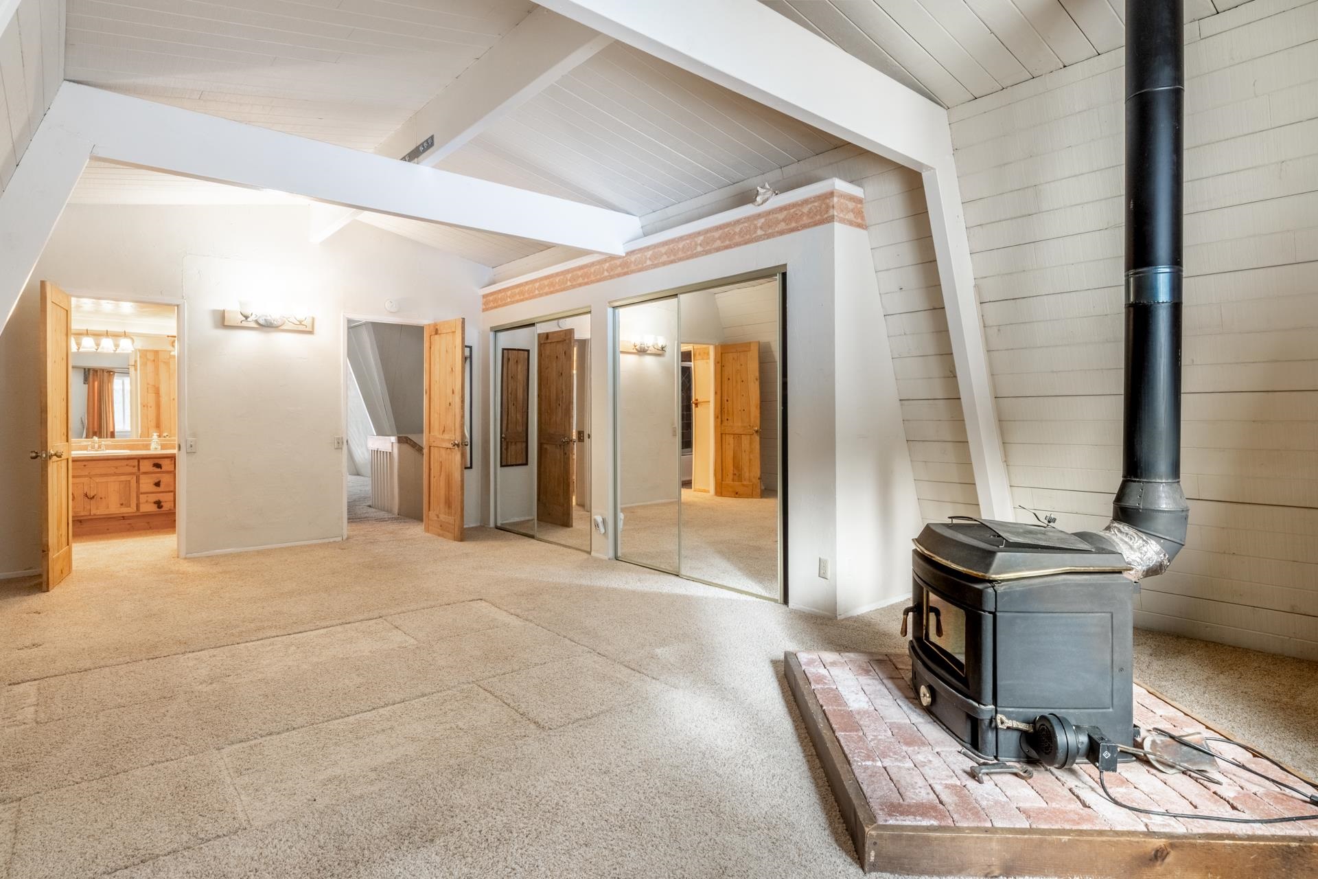 64 Mill Street Mammoth Lakes, CA 93546 - Photo 12 of 27 Unfurnished bedroom featuring a wood stove, carpet floors, two closets, ensuite bathroom, and wooden