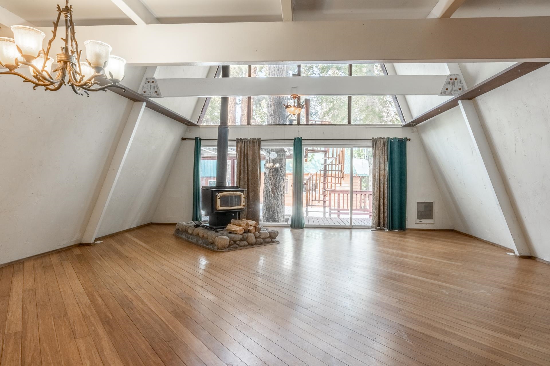 64 Mill Street Mammoth Lakes, CA 93546 - Photo 3 of 27 Unfurnished living room featuring a wood stove, hardwood / wood-style floors, heating unit, beamed ceiling, and a chandelier