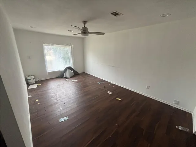 an empty room with wooden floor fan and windows