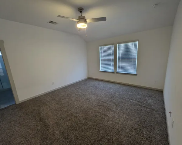an empty room with a chandelier fan and windows