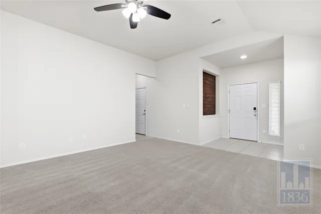 an empty room with chandelier fan and windows