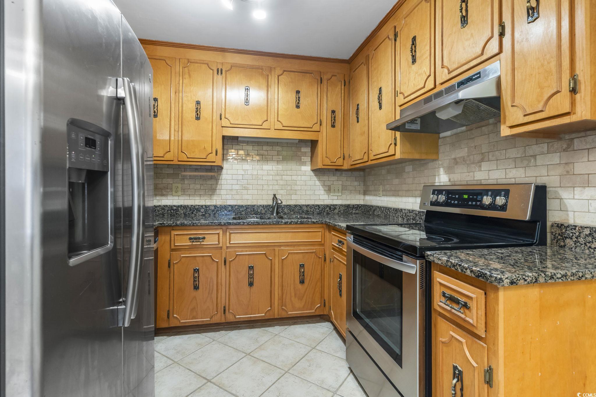 210 25th Avenue South, Unit 13 Myrtle Beach, SC 29577 - Photo 4 of 10 Kitchen with appliances with stainless steel finishes, under cabinet range hood, brown cabinets, dark stone countertops, and tasteful backsplash