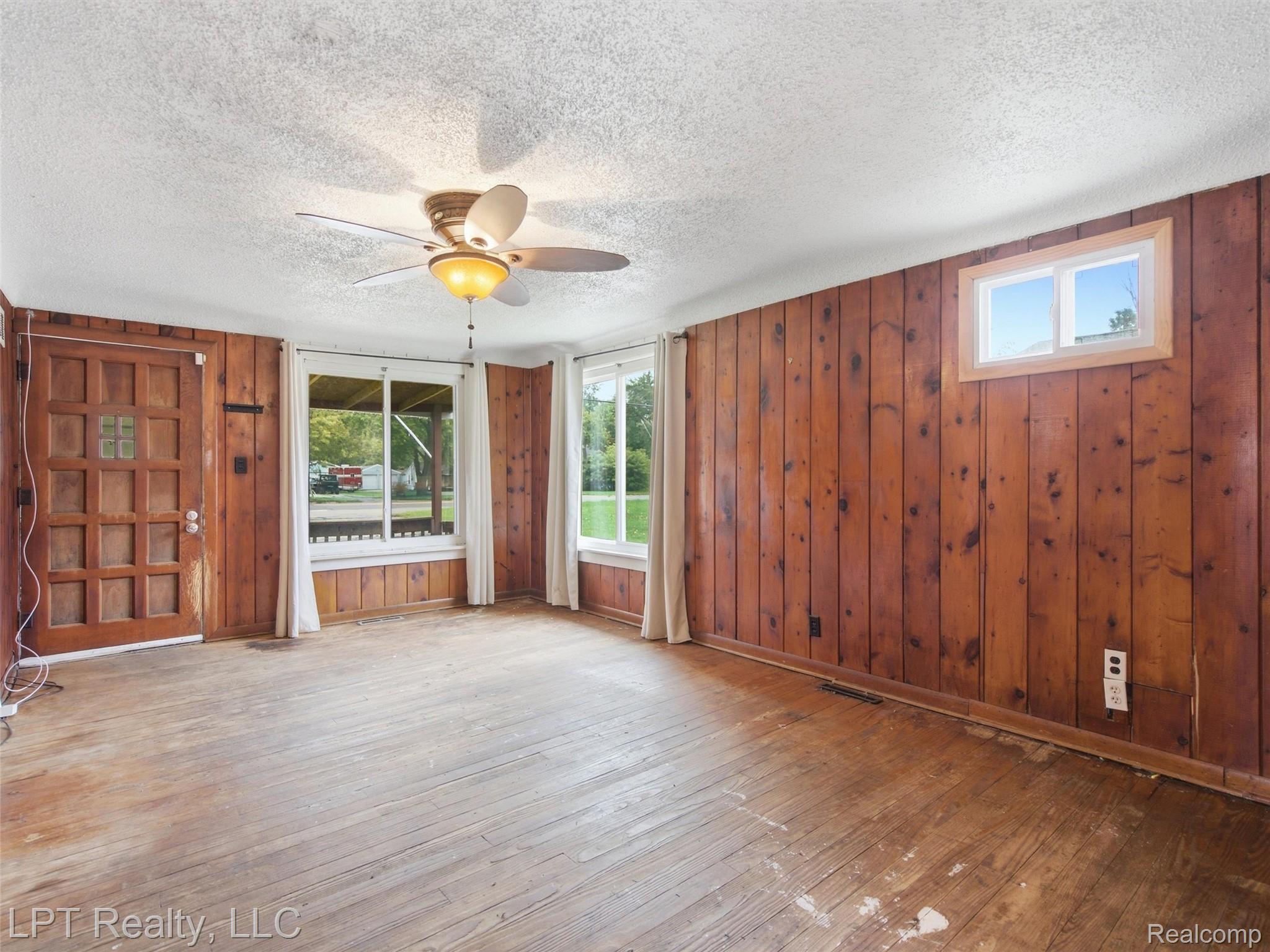3385 North Genesee Road Flint, MI 48506 - Photo 8 of 24 Wood paneling, wood-finish flooring, ceiling fan with integrated lighting, multiple windows, and a paneled wood entry door