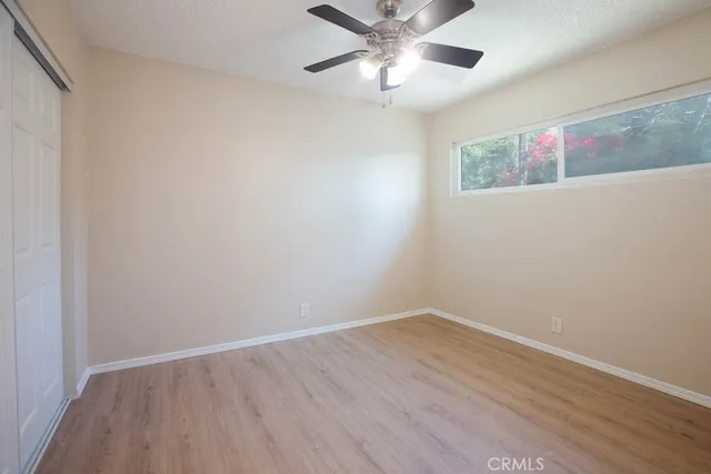 a view of an empty room with wooden floor and a ceiling fan