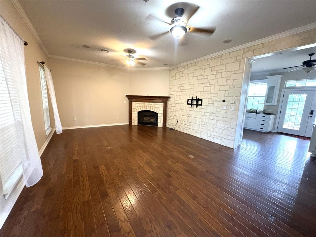 1170 Brazos Loop Gholson, TX 76705 - Photo 9 of 37 Spacious interior featuring wood-finish flooring, a stone-accented fireplace with a wood mantel, crown molding, and multiple ceiling fans