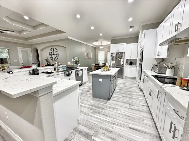 a large kitchen with stainless steel appliances kitchen island a stove a sink dishwasher and white cabinets with wooden floor