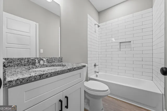 a bathroom with a granite countertop bathtub shower sink vanity and toilet