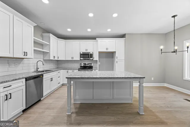 a kitchen with stainless steel appliances granite countertop a sink a stove a refrigerator and white cabinets