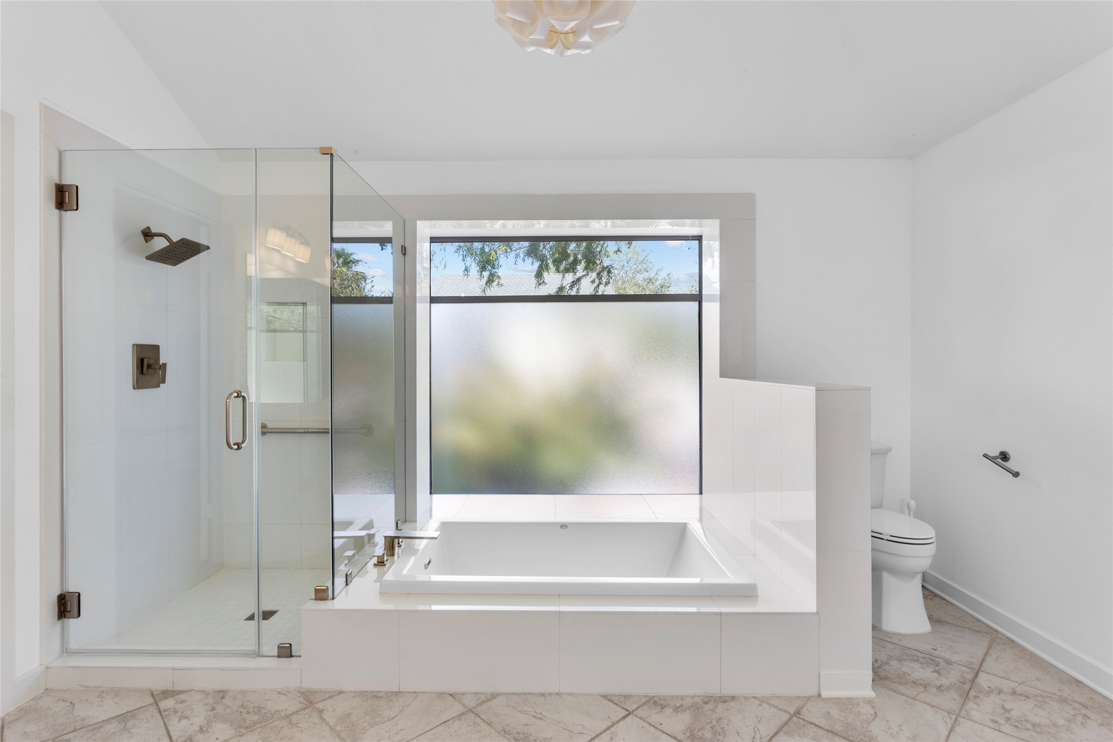67 Harbor Lane Kemah, TX 77565 - Photo 18 of 47 This Spa-like primary bathroom features a spacious design with a glass-enclosed shower and a large soaking tub. A frosted window provides natural light while ensuring privacy. The room is finished with clean, white tiles and has a modern, minimalist aesthetic.