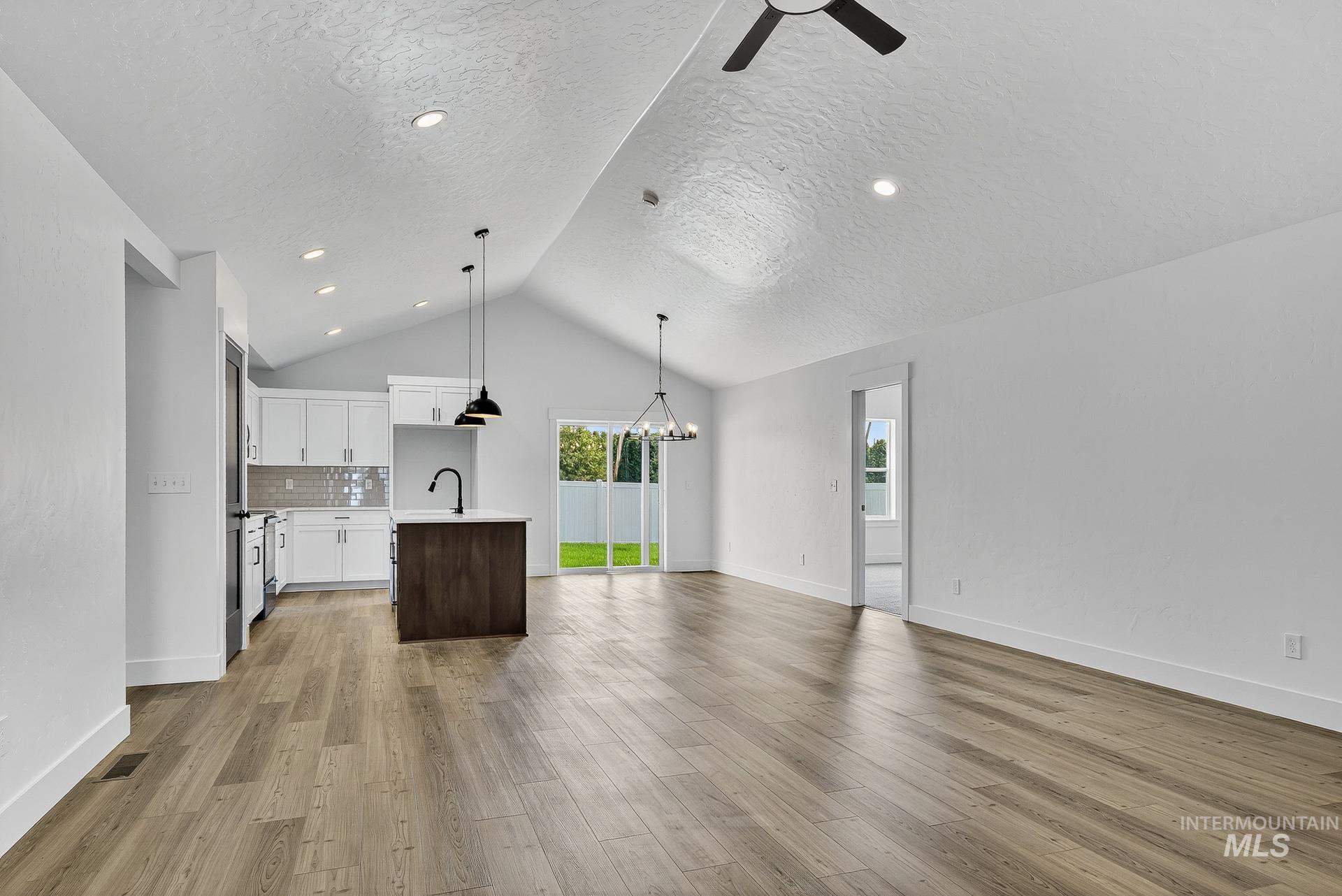1164 Velvet Loop Wilder, ID 83676 - Photo 6 of 35 Unfurnished living room featuring a chandelier, light wood-style floors, vaulted ceiling, and ceiling fan