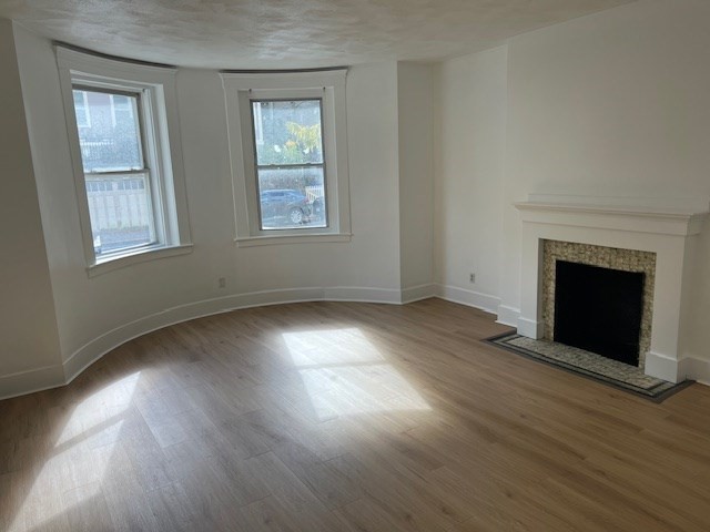 675 Washington Street, Unit 1 Brookline, MA 02446 - Photo 5 of 16 an empty room with wooden floor fireplace and windows