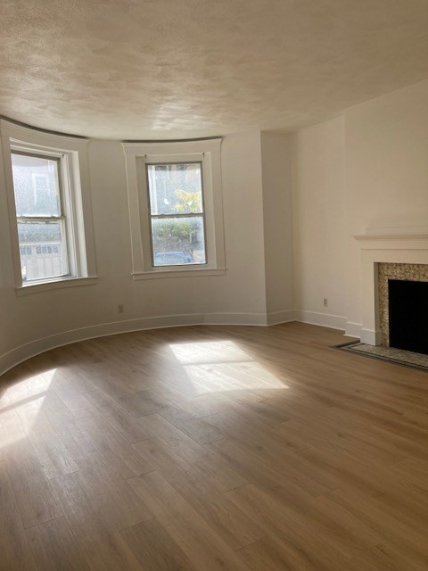 675 Washington Street, Unit 1 Brookline, MA 02446 - Photo 6 of 16 an empty room with wooden floor fireplace and windows