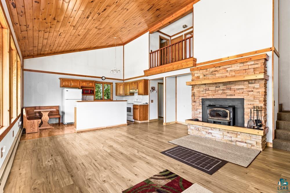 740 Seboe Road Wrenshall, MN 55797 - Photo 8 of 20 Unfurnished living room featuring light wood-type flooring, wood ceiling, baseboard heating, a stone fireplace, and high vaulted ceiling